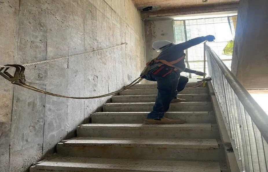 Worker wearing a safety harness beside a newly installed staircase railing inside a concrete stairwell at Bukit Merah C54 & 54A.
